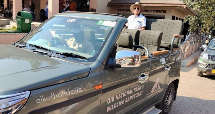 Open-top safari vehicle marked 'Gir National Park' with a tourist standing and guide driving near the visitor centre.