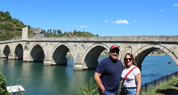 Un couple souriant devant un pont en pierre historique.