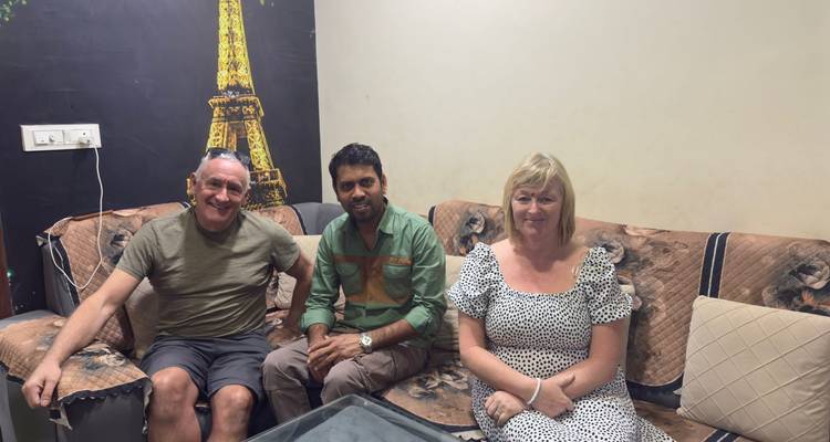 Drei Personen sitzen auf einem Sofa drinnen mit einem Wandgemälde des Eiffelturms hinter ihnen.