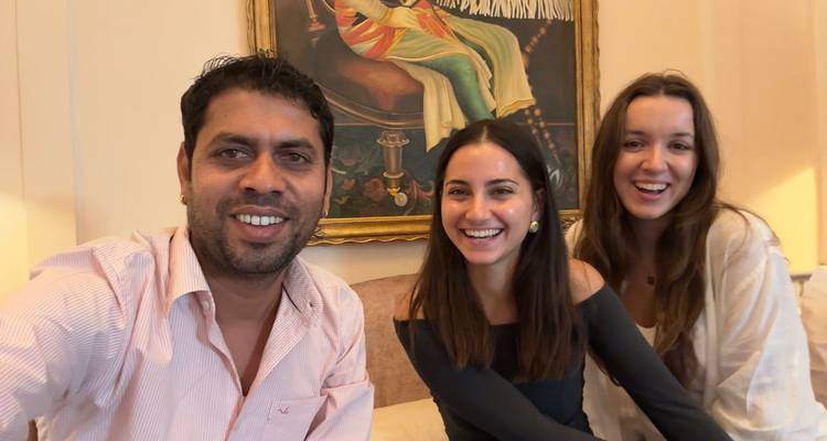 Drei Menschen lächeln vor einem dekorativen Gemälde in Innenräumen.