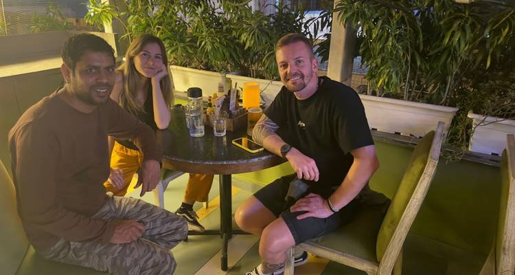 Drei Personen sitzen an einem Tisch in einer Außenumgebung.