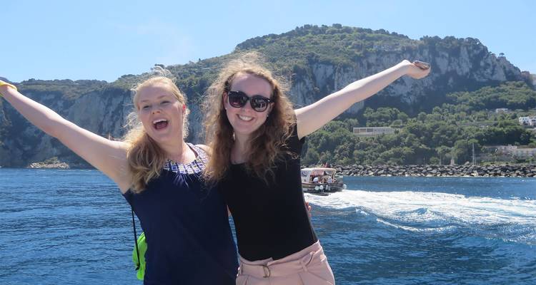 Deux femmes les bras levés profitant d'une balade en bateau avec des falaises derrière.