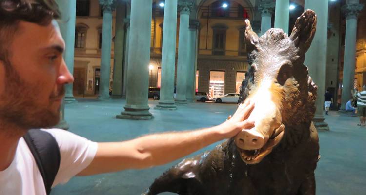 Una persona tocando el hocico de una estatua de bronce de jabalí bajo un arco.