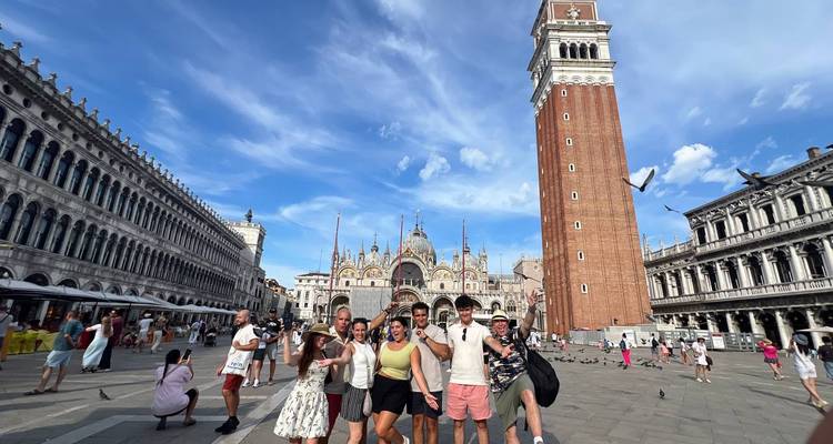 Groupe de touristes posant sur une place avec une basilique et une haute tour à Venise.