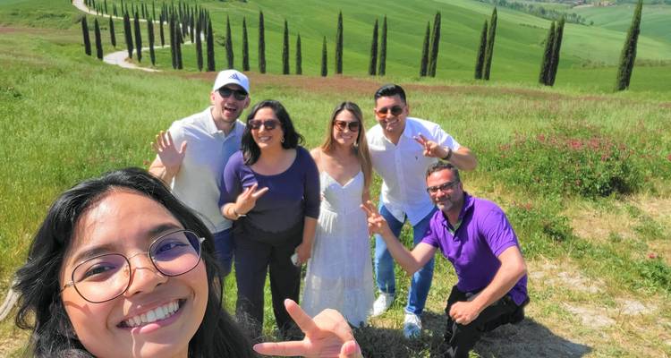 Groupe de personnes souriantes prenant un selfie dans un paysage pittoresque avec des cyprès.