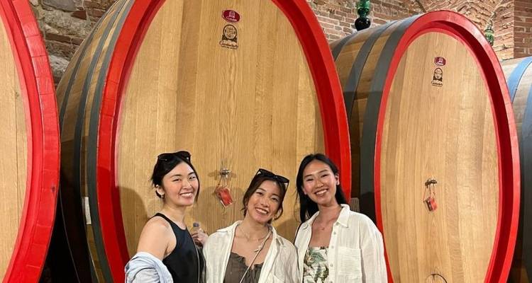 Trois femmes debout dans une cave à vin avec de gros tonneaux.