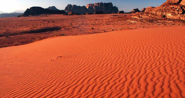 Woestijnlandschap met geribbelde zandduinen en bergen in de verte.