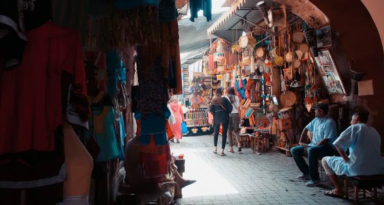 Des gens faisant leurs courses dans une ruelle de marché étroite avec des marchandises suspendues.