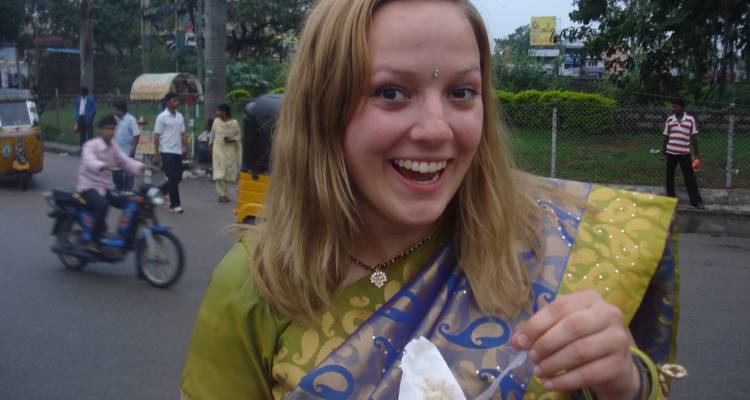 Smiling person holding a snack in a busy street wearing traditional attire.