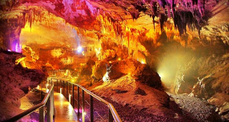 Cueva iluminada con estalactitas y un sendero para caminar.