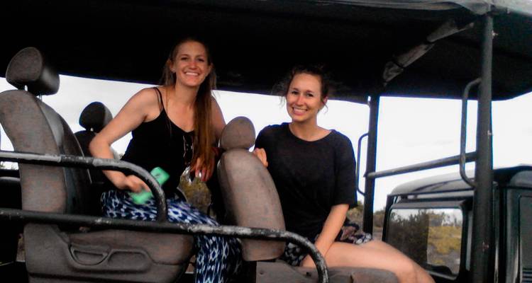Two women sitting on seats in an open jeep-like vehicle.