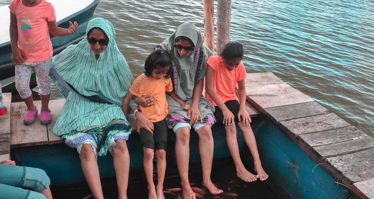 Group of people sitting on a wooden platform with feet in water.
