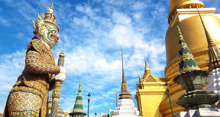 Statue eines Wächterdämons im Wat Phra Kaew mit goldener Stupa im Hintergrund.