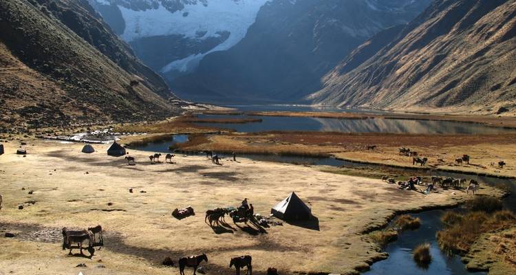 Campsite with people and animals by a river in the mountains.