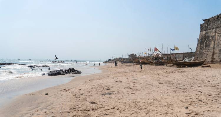 Una playa de arena con gente, barcos y banderas a lo largo de la orilla.