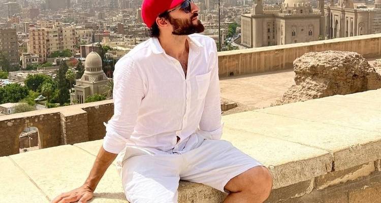 Mann mit roter Mütze sitzt auf einer Steinmauer mit Kairo im Hintergrund.