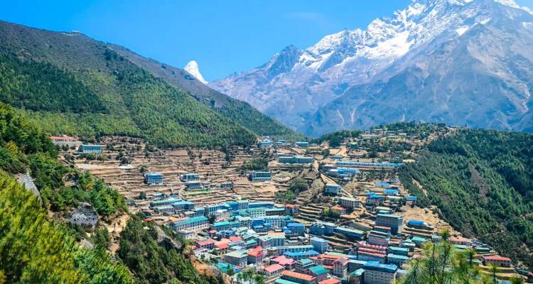 Farbenfrohe, terrassenförmig angelegte Stadt Namche Bazaar vor majestätischen schneebedeckten Gipfeln an einem klaren Tag.