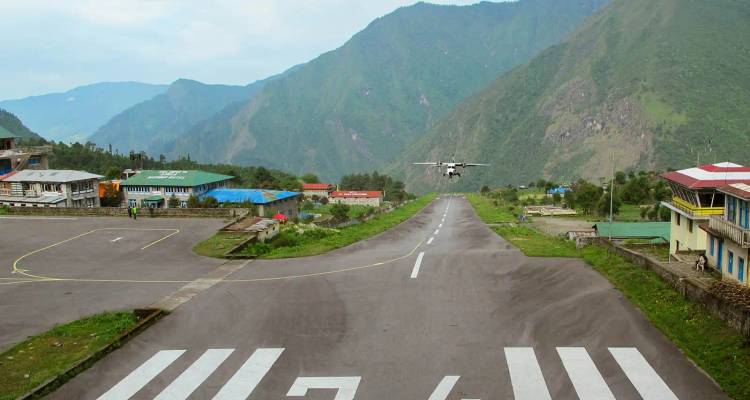 Flugzeug, das auf der kurzen Gebirgsstartbahn des Flughafens Lukla landet, umgeben von grünen Hügeln.