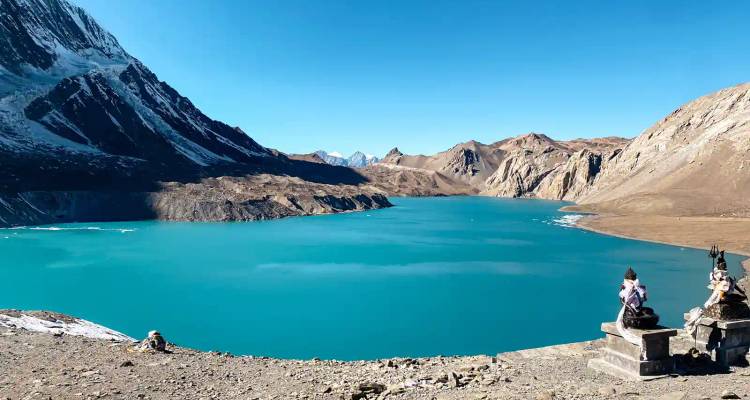 Briljant turquoise alpien meer omringd door kale bruine bergen onder een helder blauwe lucht.