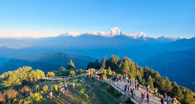 Groep wandelaars op een houten uitkijkplatform met uitzicht op de lagen van Himalaya-bergketens bij zonsopgang.