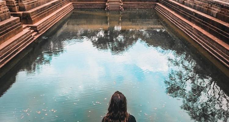 Person, die an einem reflektierenden Wasserbecken sitzt, umgeben von alten Steinstufen.
