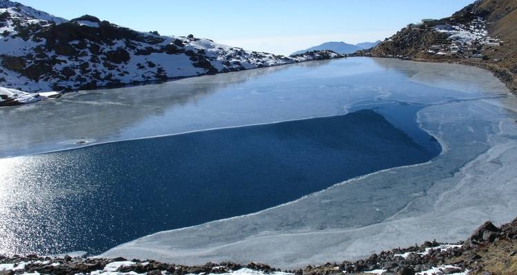 Lac partiellement gelé dans une vallée de montagne avec un ciel dégagé.