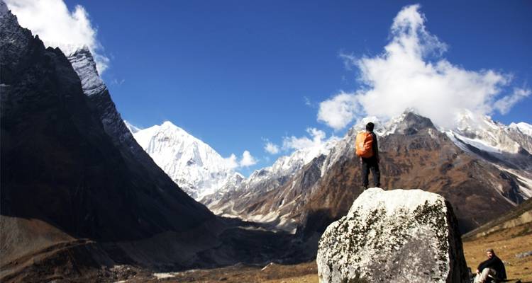 Person standing on a rock in front of snow-covered mountains.