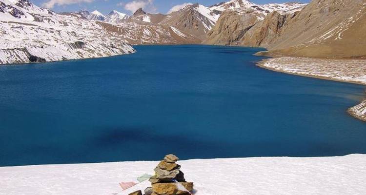 Lac bleu clair entouré de neige, situé dans un paysage de montagne.