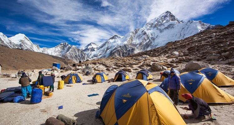 Un camping avec plusieurs tentes installées sur fond de montagnes enneigées, avec quelques personnes qui s'installent et se détendent.