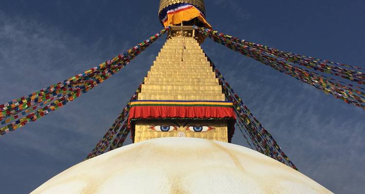 Boudhanath Stupa with colorful prayer flags against a blue sky.