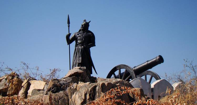 Statue eines Kriegers und einer Kanone auf felsigem Gelände.