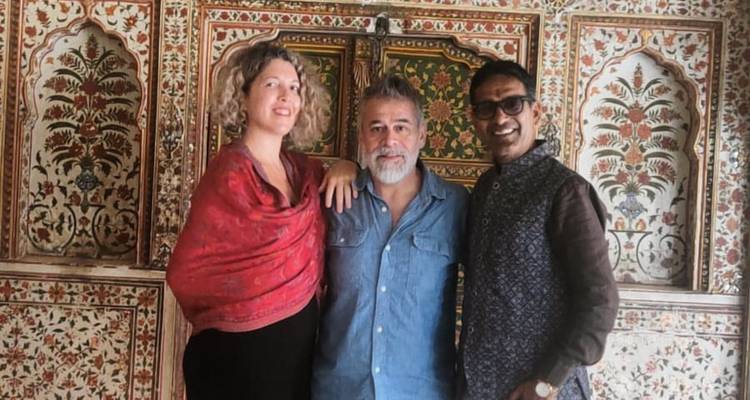 Three people posing in front of a richly decorated wall.