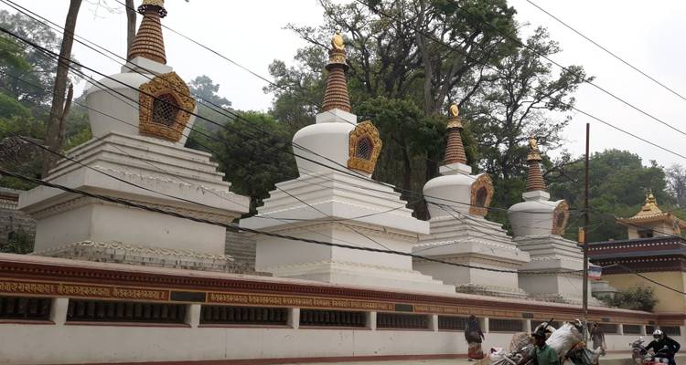 Reihe weißer Stupas mit kunstvollen goldenen Spitzen, die sich entlang einer Straße mit Überlandleitungen erstrecken