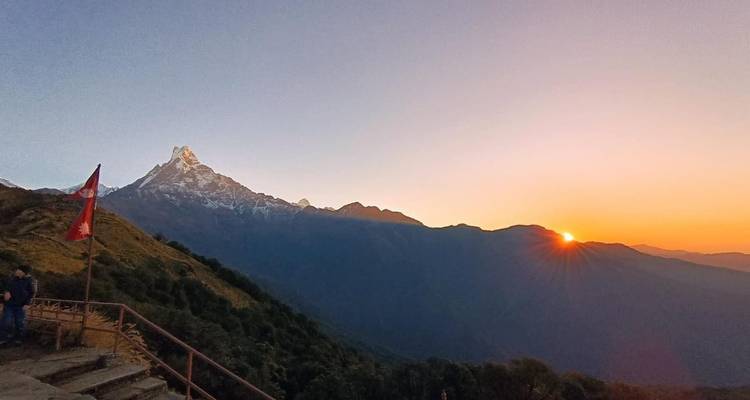 Le soleil se lève derrière les pics lointains de l'Himalaya tandis qu'un observateur solitaire se tient près d'un belvédère sur le flanc d'une colline avec un drapeau népalais.