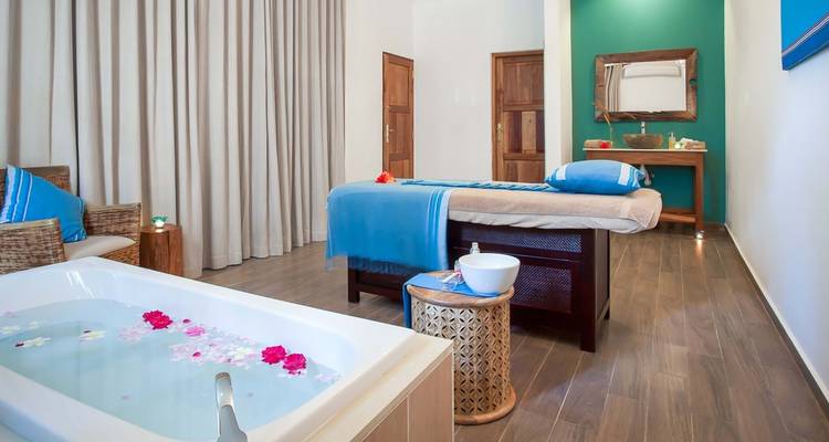 Spa-Raum mit einer Massageliege und einer Wanne voller Blütenblätter.