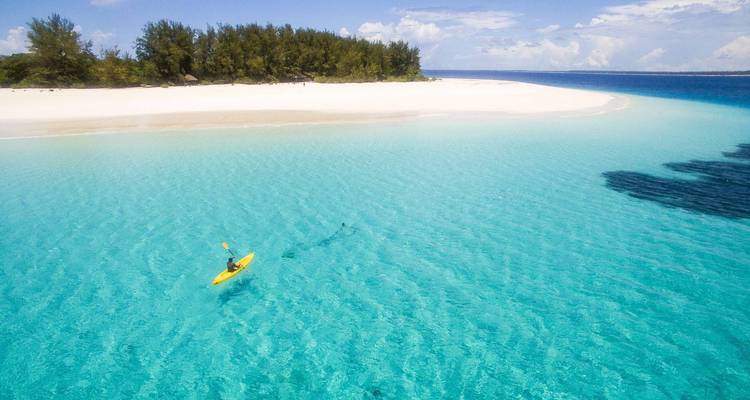 Kajakfahrer paddelt in klarem türkisfarbenem Wasser in der Nähe eines weißen Sandstrandes.