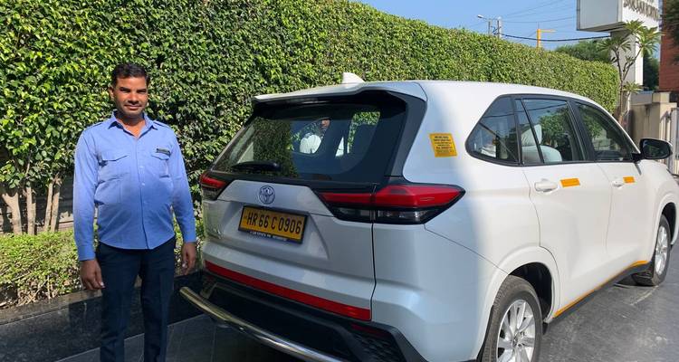 Chauffeur debout fièrement à côté d'un SUV touristique blanc avec plaque d'immatriculation jaune.
