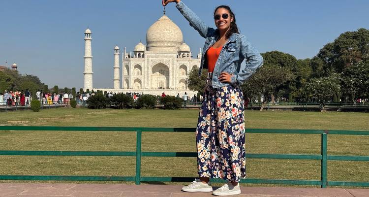 Jeune femme crée une pose en perspective forcée avec le Taj Mahal entre le pouce et l'index par une journée ensoleillée.