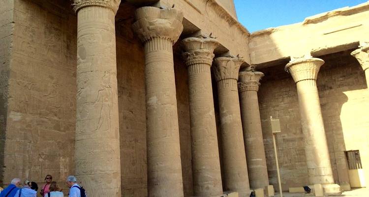 Fila de enormes columnas de piedra talladas ornamentalmente dentro de un antiguo templo con un cielo azul brillante arriba.