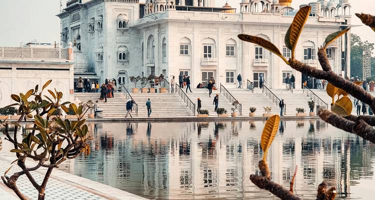 Witte marmeren Sikh gurdwara naast een reflecterend bassin met bezoekers die langs de trappen lopen in Delhi.