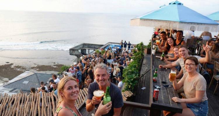 Grupo de personas disfrutando bebidas en una terraza con vista al océano.