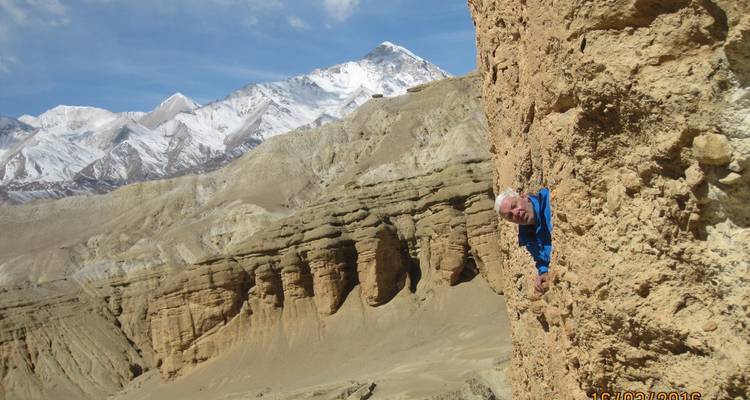 Man playfully peeping out from rock formations in a mountainous landscape.