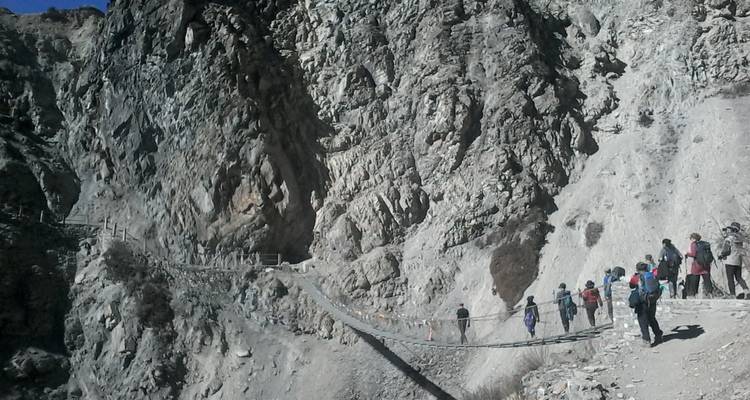 Wanderer überqueren eine Hängebrücke inmitten felsigen Geländes.