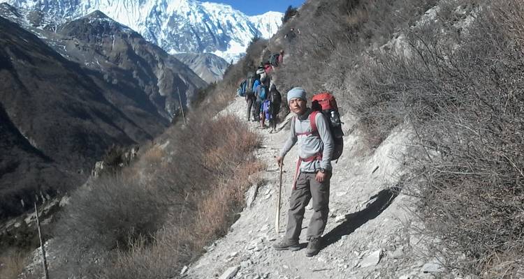 Gruppe von Wanderern auf einem Bergpfad mit schneebedeckten Gipfeln im Hintergrund.