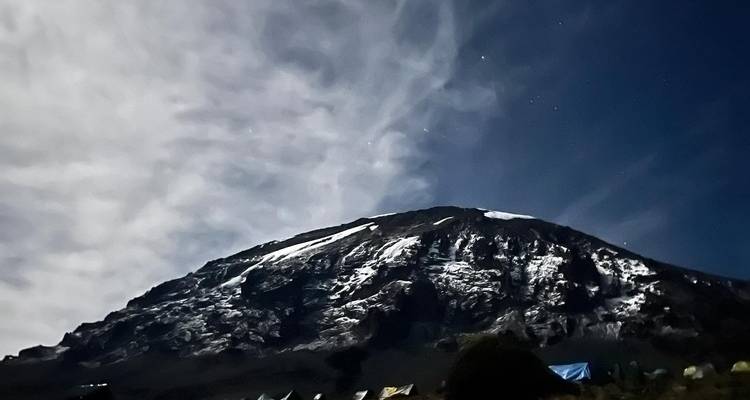 Vue de montagne sous un ciel étoilé nocturne avec des tentes visibles.