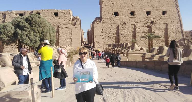 Lächelnde Frau, die ein Touristenschild bei antiken Ruinen hält.