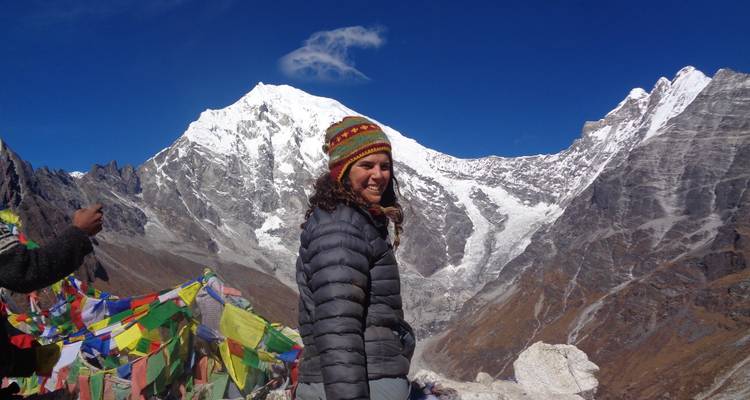 Personne debout avec des drapeaux de prière et des montagnes enneigées.