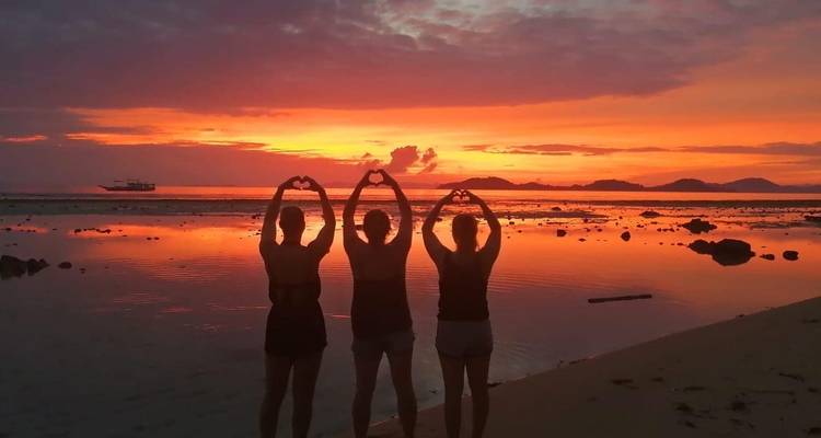 Tres personas haciendo formas de corazón with sus manos durante una puesta de sol dramática en la playa.