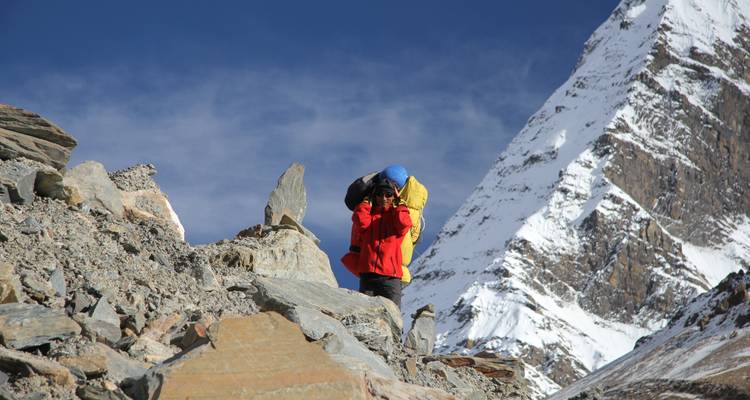 Wandelaar met rugzak op rotsachtig terrein met besneeuwde berg op de achtergrond.