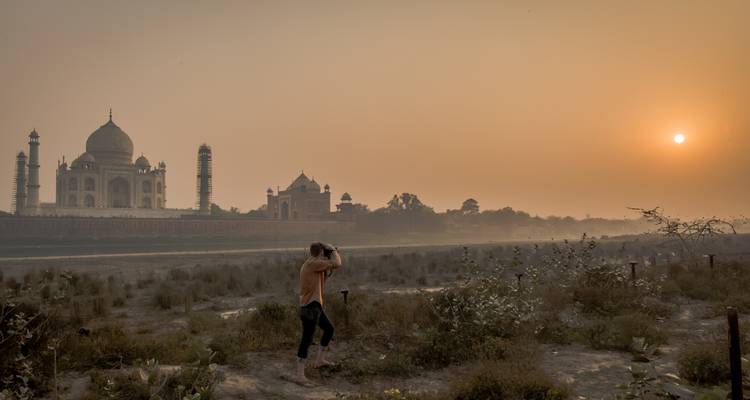 Bezoeker die het zonsopgangzicht van de Taj Mahal aan de overkant van de rivier vastlegt.